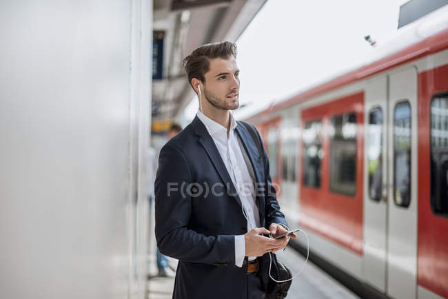 Homme d'affaires à la station avec écouteurs et téléphone portable — Photo de stock