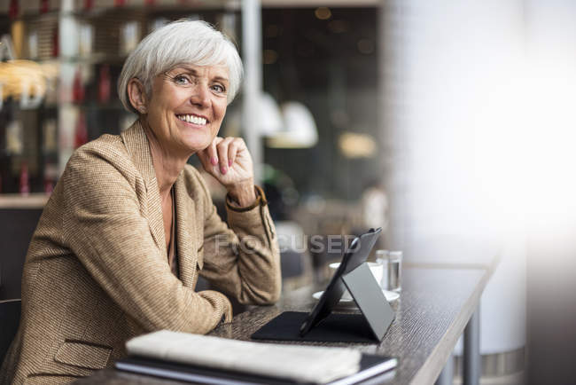 Retrato de mujer de negocios mayor sonriente sentada con la tableta en la cafetería - foto de stock