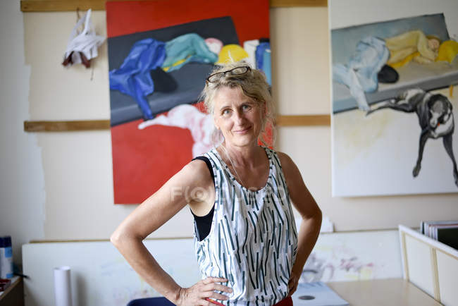 Femme peintre adulte dans son atelier posant sur la caméra, photos sur le mur — Photo de stock