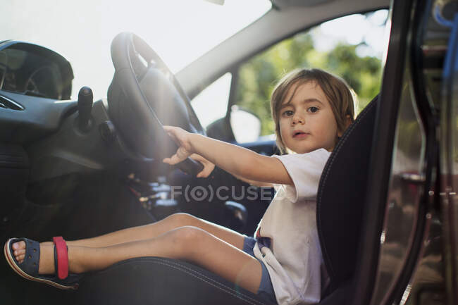 Retrato del niño sentado en el asiento del conductor en un coche - foto de stock