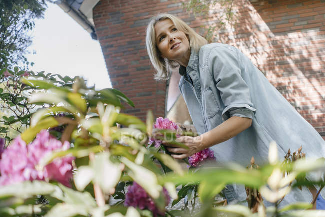 Lächelnde reife Frau mit Blumen im Garten — Stockfoto