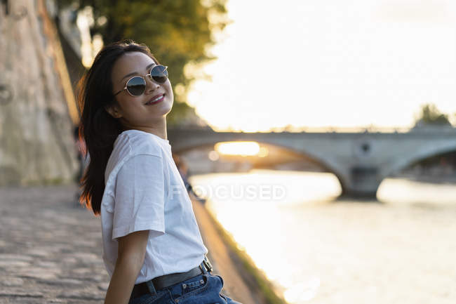 France, Paris, portrait of smiling young woman with sunglasses at river Seine at sunset — Stock Photo
