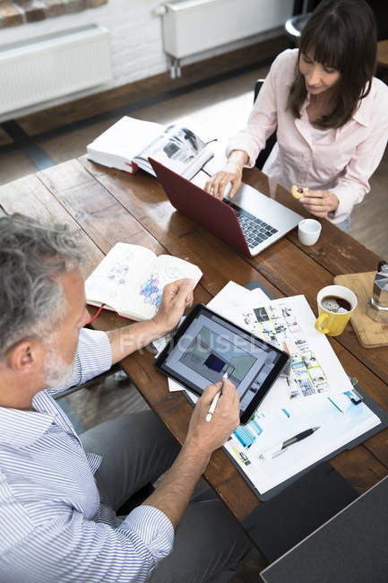 Mature couple working from their home office, using laptop and digital tablet — Stock Photo