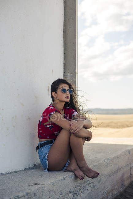 Ritratto di ragazza adolescente che indossa occhiali da sole seduta sul muro e guarda la distanza — Foto stock