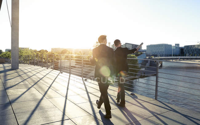Dos hombres de negocios caminando por un puente en la ciudad - foto de stock