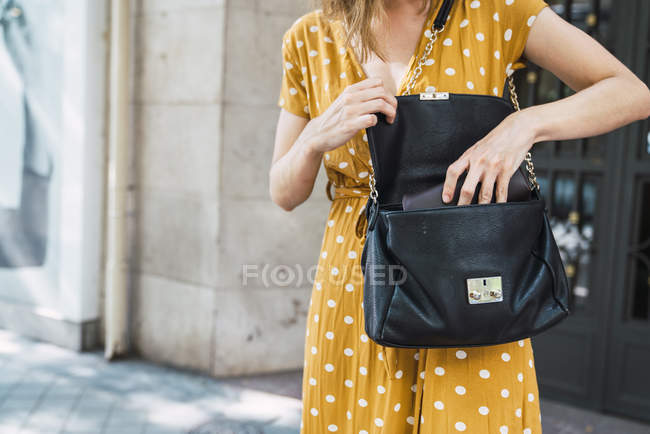 Woman in yellow dress with polka dots opening shoulder bag — Stock Photo