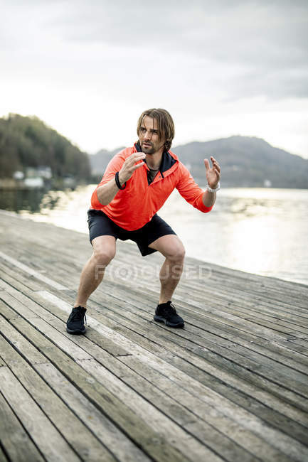 Atleta haciendo ejercicio en cubierta de madera en la orilla del lago - foto de stock