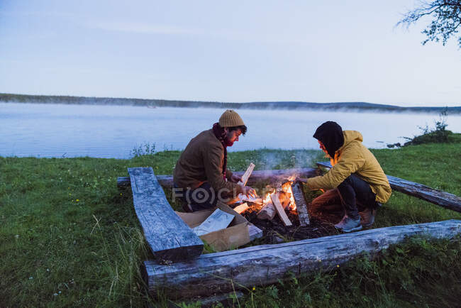 Suecia, Laponia, Dos amigos preparando una hoguera en la orilla del lago - foto de stock