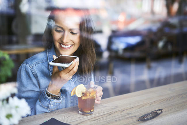 Smiling young woman speaking on phone in cafe while having tea — Stock Photo