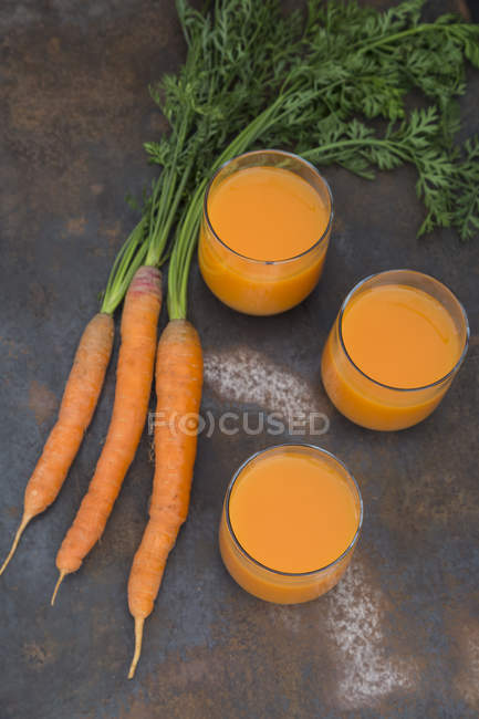 Tre bicchieri di succo di carota fresco e tre carote — Foto stock