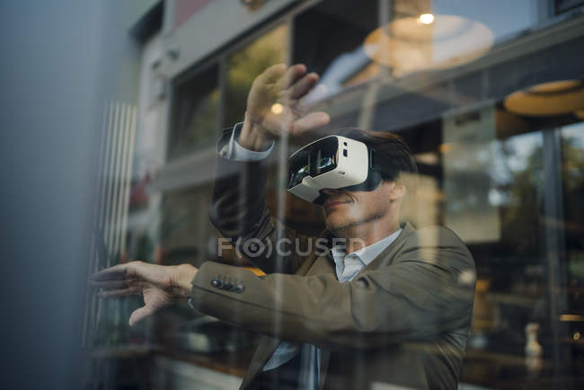 Mature businessman sitting in coffee shop, looking through VR glasses — Stock Photo