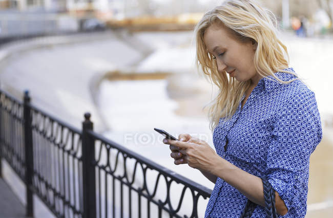 Mujer rubia en puente usando smartphone - foto de stock
