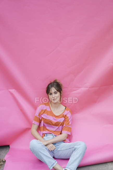 Selbstbewusste junge Frau sitzt auf rosa Hintergrund — Stockfoto