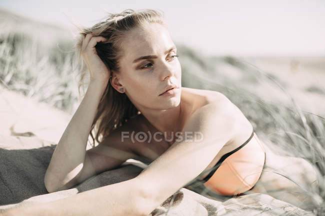 Ritratto di una giovane donna sdraiata in spiaggia duna sabbiosa e distogliendo lo sguardo — Foto stock