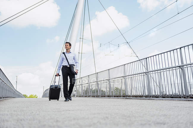Бизнесмен с чемоданом катится через мост — стоковое фото