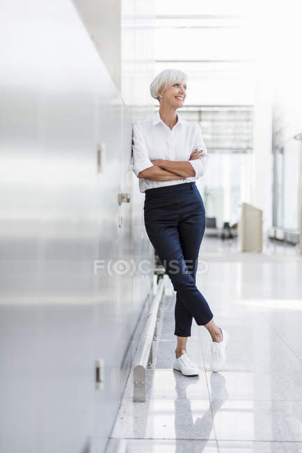 Femme d'affaires âgée souriante appuyée contre le mur — Photo de stock