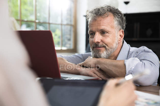 Зрілий чоловік за допомогою ноутбука, жінка з цифровим планшетом. — стокове фото