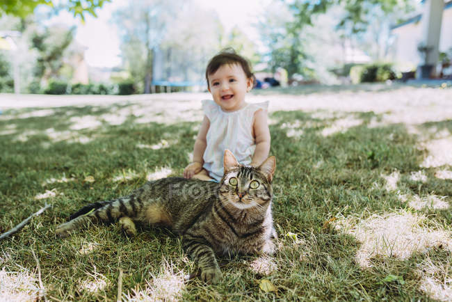 Ritratto di gatto tabby su un prato con bambina che ride seduta sullo sfondo — Foto stock