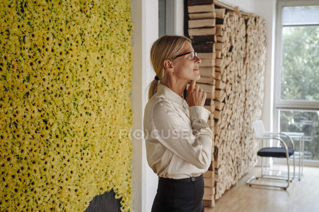 Imprenditrice in ufficio a parete con girasoli pensando — Foto stock