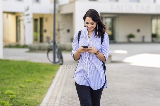 Retrato del estudiante sonriente usando teléfonos inteligentes y auriculares al aire libre - foto de stock