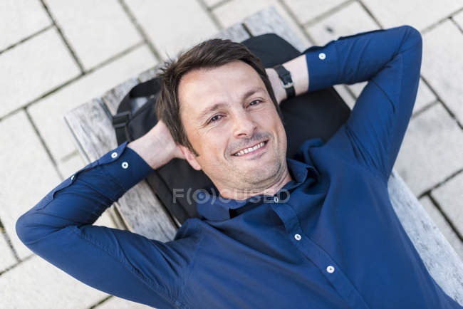 Porträt eines lächelnden Geschäftsmannes, der auf einer Bank im Freien liegt — Stockfoto