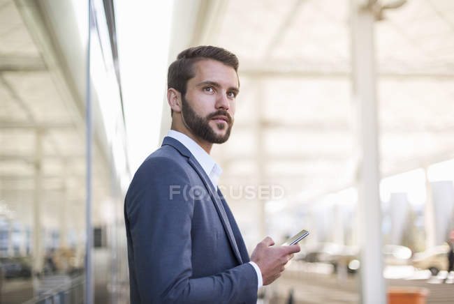 Joven hombre de negocios sosteniendo el teléfono celular mirando hacia los lados - foto de stock