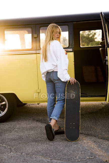 Giovane donna con skateboard in piedi al di fuori di un furgone vintage — Foto stock