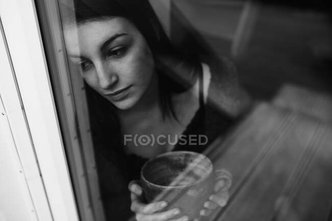 Retrato de jovem com xícara de chá olhando pela janela — Fotografia de Stock