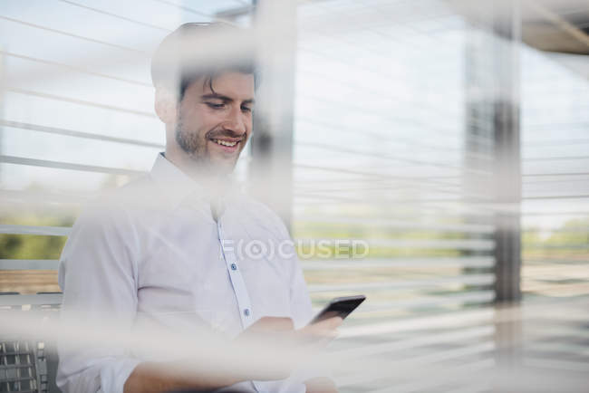 Uomo d'affari sorridente sulla piattaforma della stazione utilizzando il telefono cellulare — Foto stock