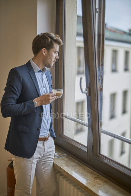 Бізнесмен з чашкою кави дивиться з вікна — стокове фото