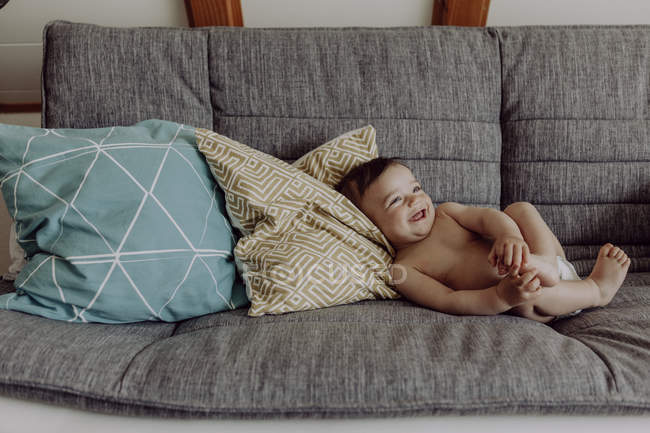 Сміється дитина хлопчик лежить на дивані вдома — стокове фото
