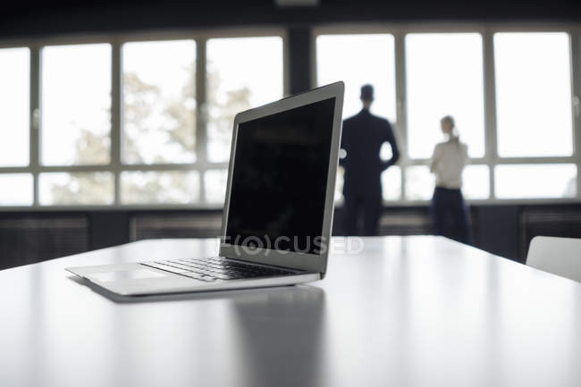 Laptop na mesa e homem de negócios e mulher de negócios na janela — Fotografia de Stock