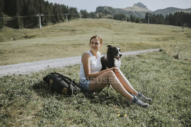 Áustria, Vorarlberg, Mellau, mulher com cão sentado na grama nas montanhas — Fotografia de Stock