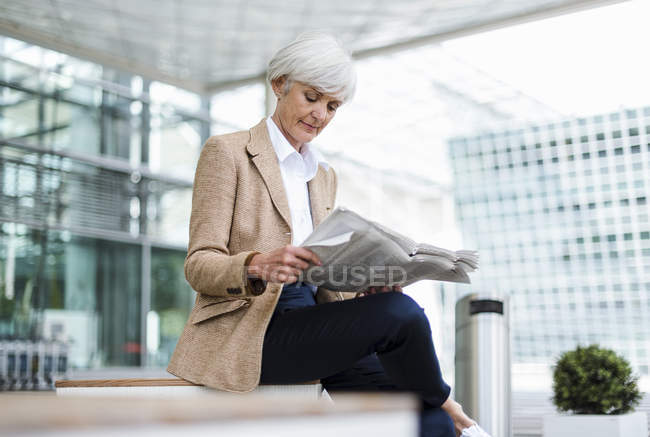 Senior businesswoman sitting in city and reading newspaper — Stock Photo