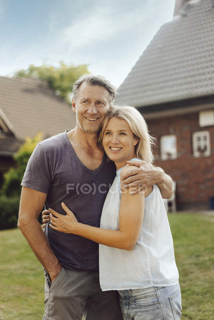 Portrait of smiling mature couple embracing in garden of house — Stock Photo