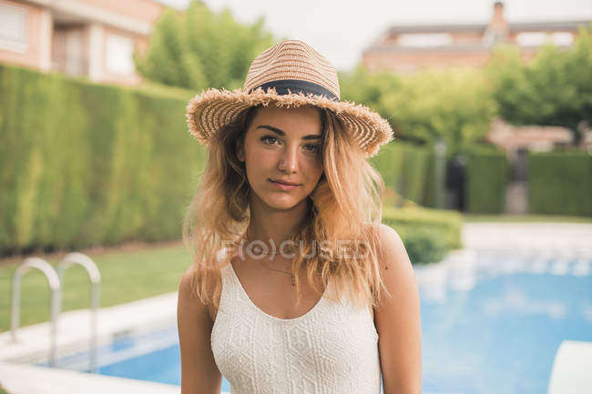 Портрет молодої жінки з солом'яним капелюхом і купальнику, басейн у фоновому режимі — стокове фото