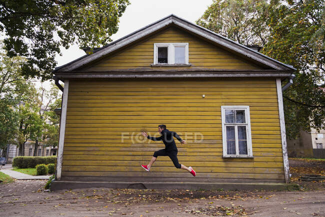 Динамичный спортсмен прыгает перед домом из желтого дерева — стоковое фото