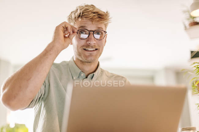 Giovane uomo utilizzando il computer portatile e guardando attraverso gli occhiali — Foto stock