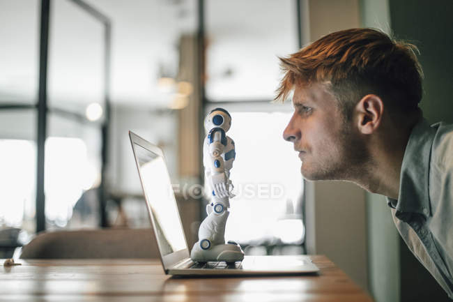 Uomo guardando robot giocattolo, in piedi sul computer portatile — Foto stock
