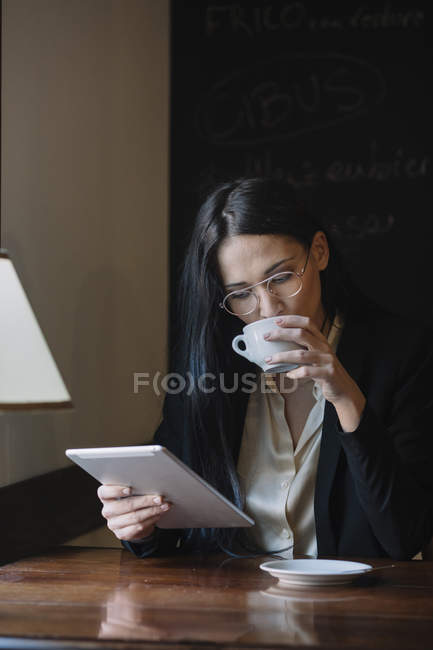 Молода бізнес-леді п'є каву і використовує таблетки в кафе — стокове фото