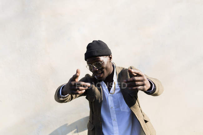 Jeune homme au chapeau laineux gesticulant devant le mur — Photo de stock