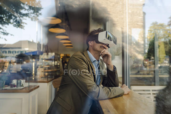 Homme d'affaires mature assis dans un café, regardant à travers des lunettes VR — Photo de stock