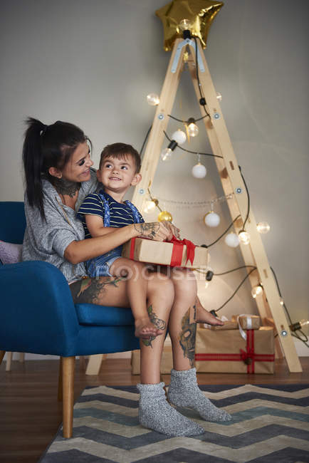Happy boy opening Christmas present with his mother at home — Stock Photo