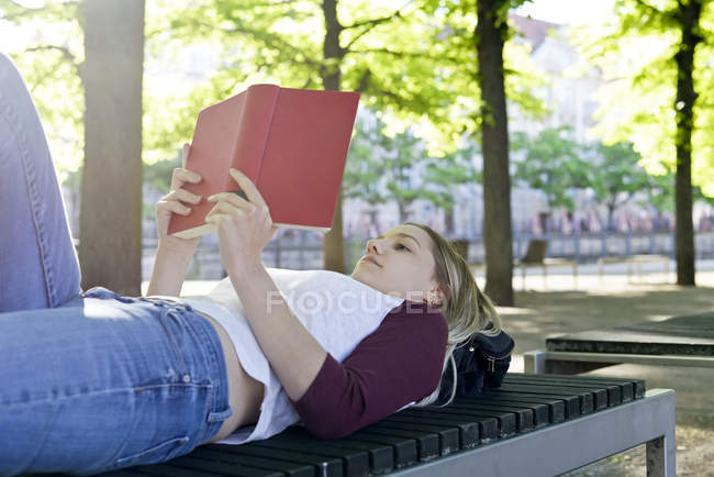 Mujer joven leyendo un libro en el banco - foto de stock