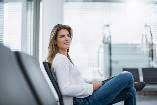 Молодая деловая женщина сидит в зале ожидания с планшетом — стоковое фото