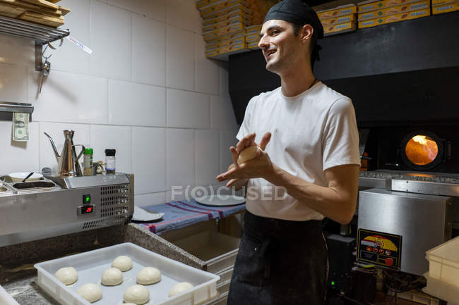 Smiling pizza baker shaping dough in kitchen — Stock Photo