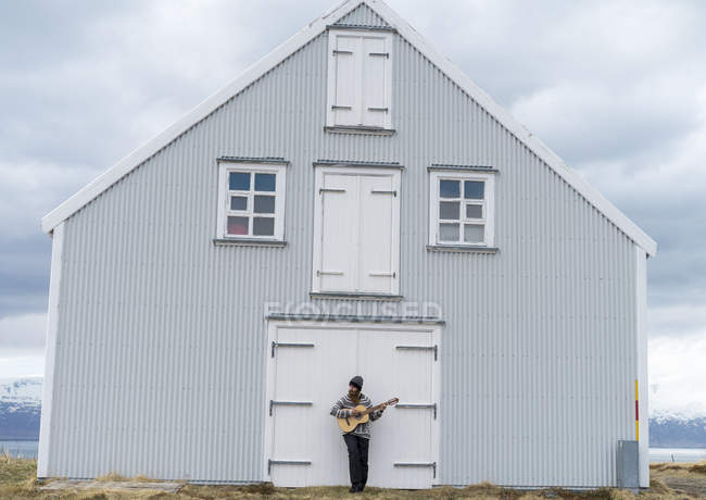 Islandia, joven tocando la guitarra, casa de madera - foto de stock