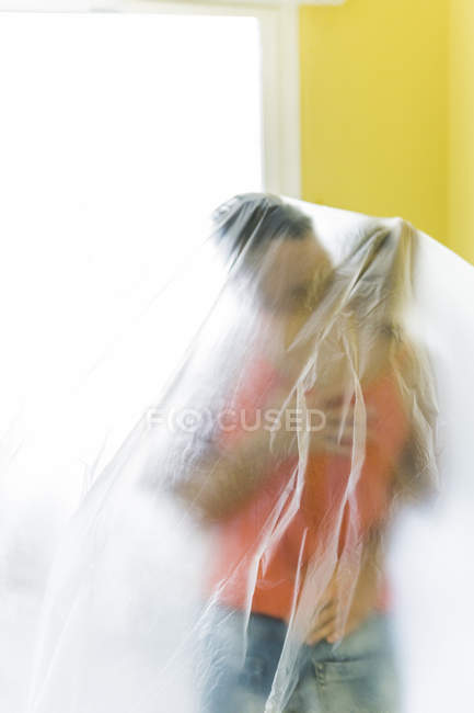 Baciare coppia sotto pellicola di plastica a casa nuova — Foto stock