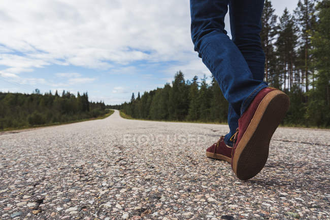 Vue partielle des jambes de l'homme, les pieds de l'homme marchant sur la route de campagne vide — Photo de stock