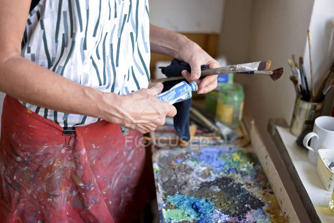 Pintora en su taller, tubo de pintura y pinceles - foto de stock